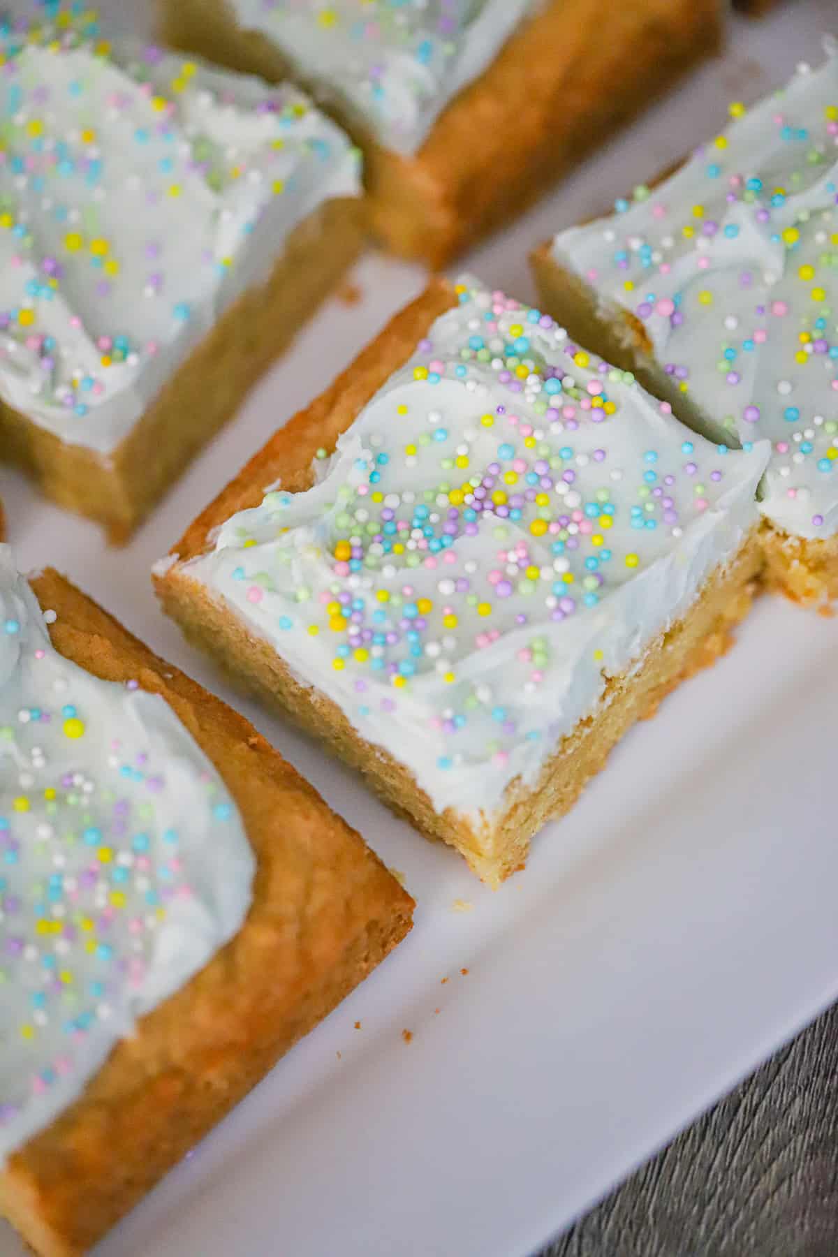 Spring sprinkle cookie bars with green buttercream frosting cut into squares on parchment paper