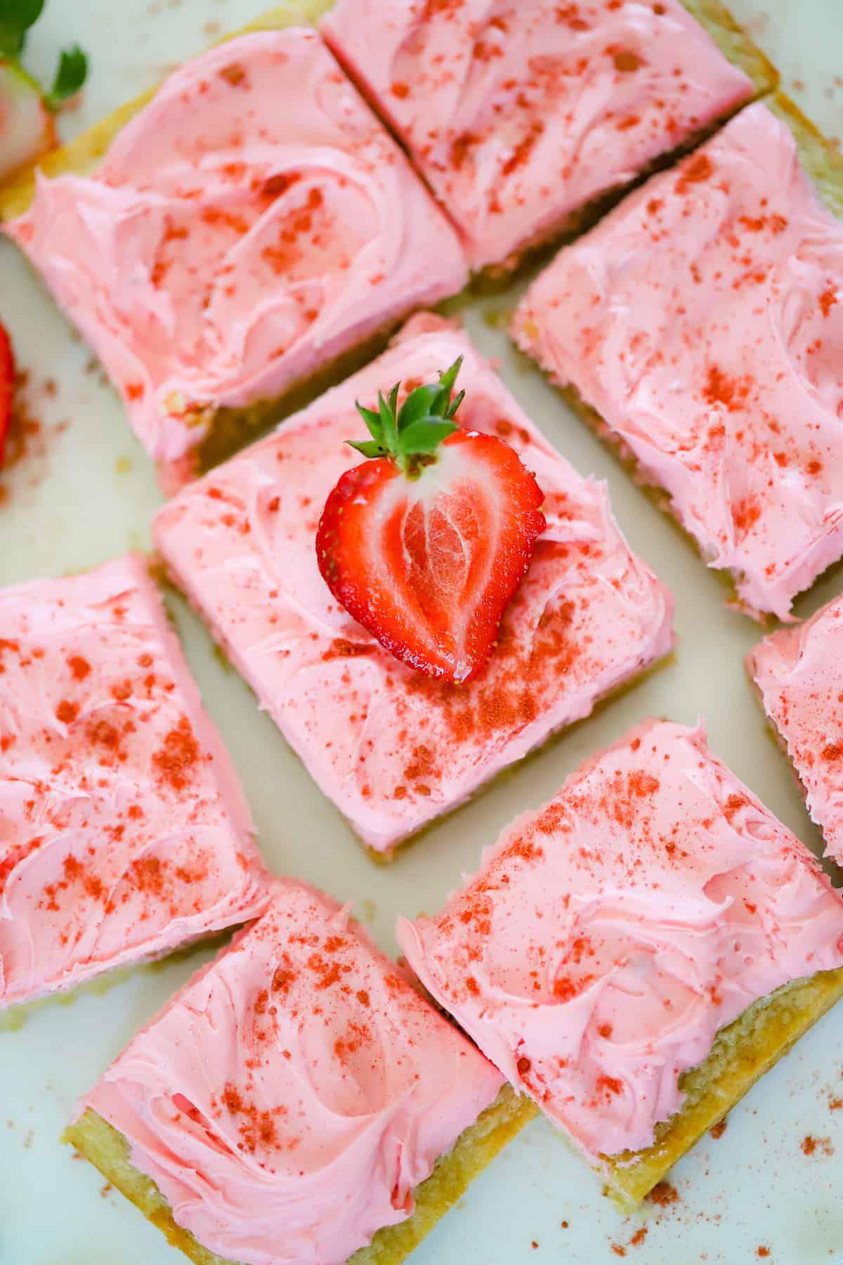 Buttery brown sugar bars with pink frosting being sliced on a cutting board