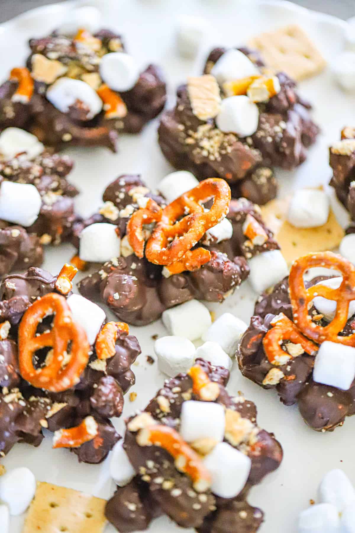No bake s'mores pretzel clusters stacked on parchment with melted chocolate and mini marshmallows