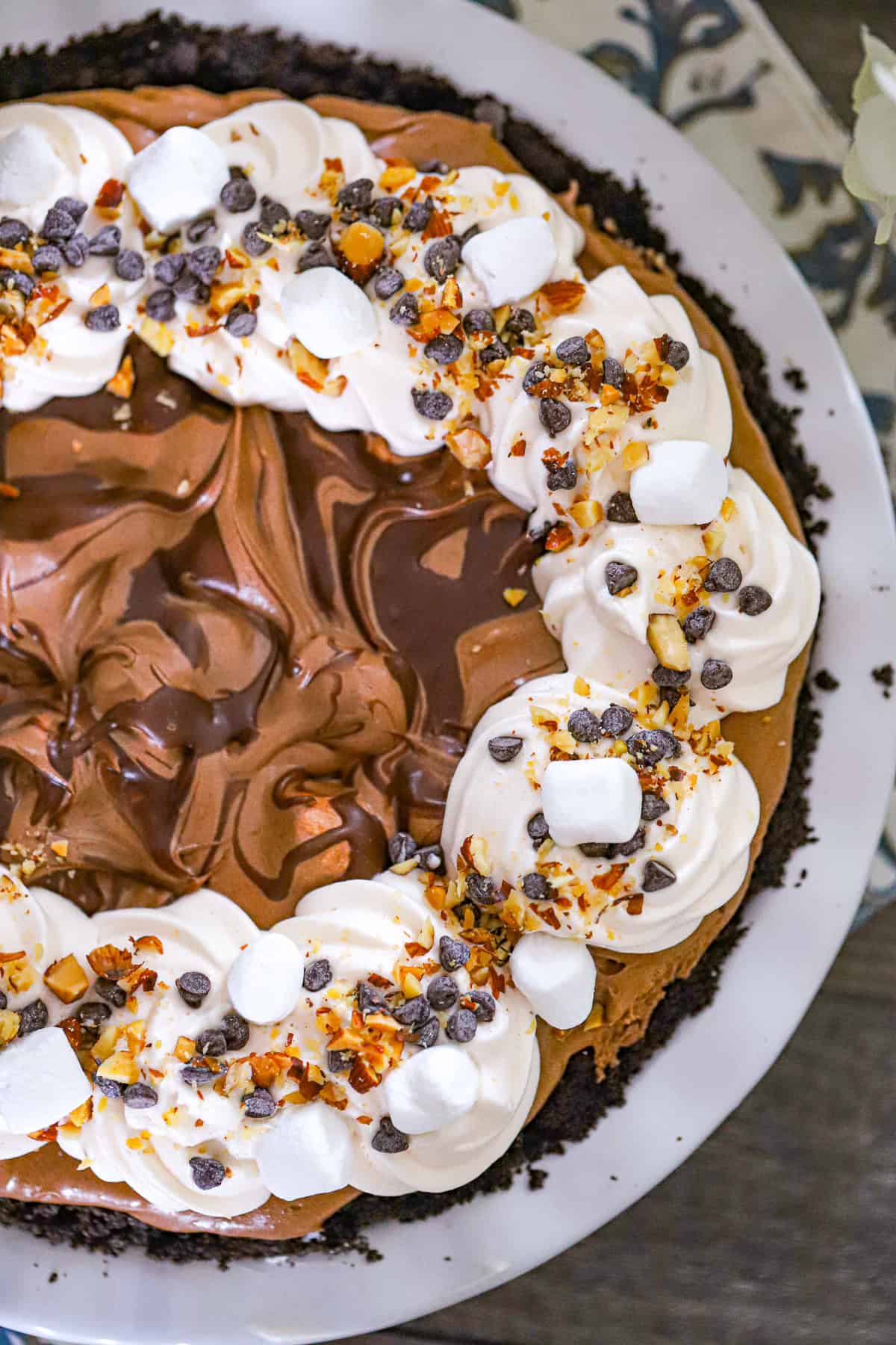 Tall chocolate pie topped with mini marshmallows chopped nuts and chocolate chunks