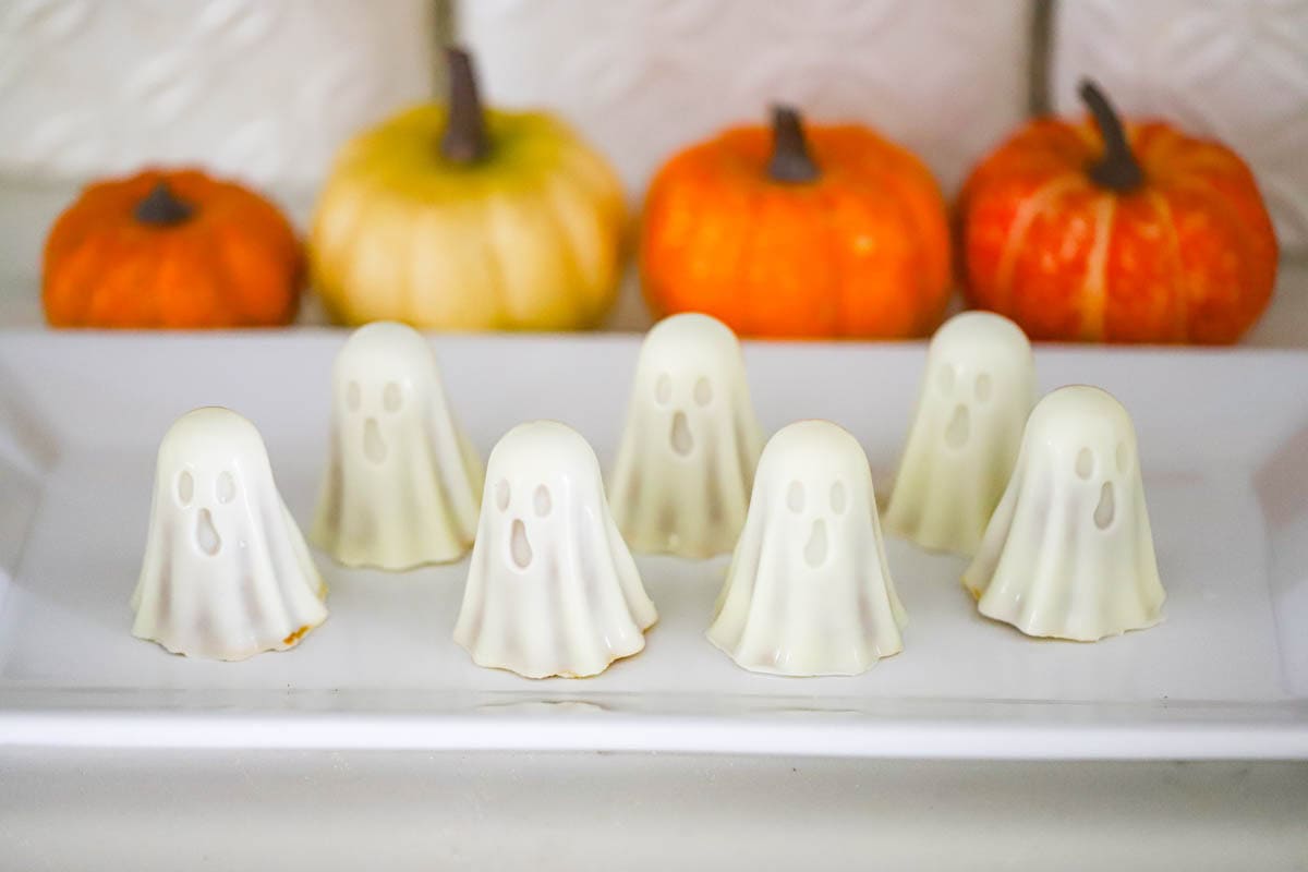 White Chocolate Ghost Truffles lined up with colorful pumpkins in the background